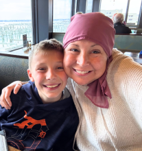 Jen is hugging her child, posing for a photo in a restaurant with large windows in the background
