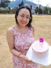 Stefania celebrates the fifth anniversary of transplant for aplastic anemia and PNH. She is holding a cake with the large number "5" as she shows it to the photographer.